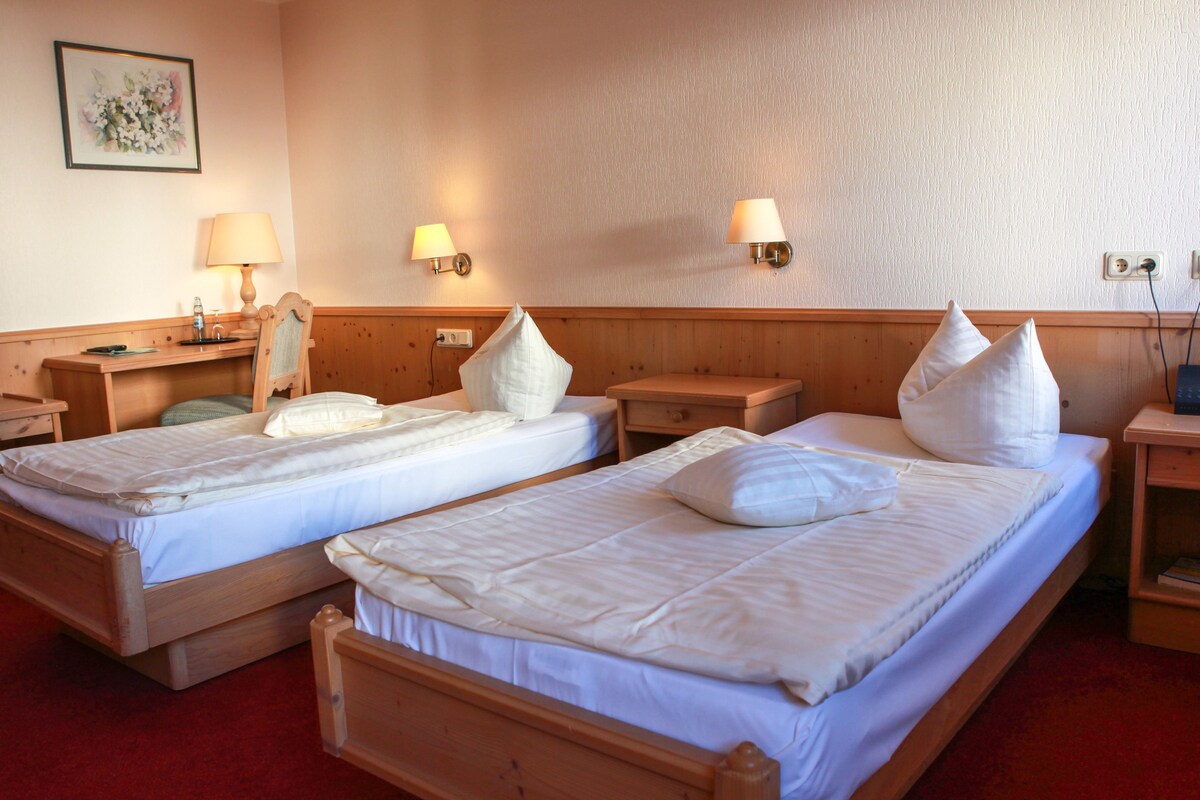 A hotel room with two beds, bedside tables, lamps, a desk, and a chair.