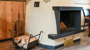 Een stenen open haard met een zwarte omlijsting en een houten bankje aan de linkerkant.