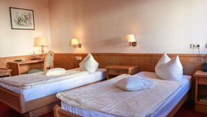 Een hotelkamer met twee enkele bedden, houten hoofdborden, nachtkastjes met lampen, een bureau en een stoel.