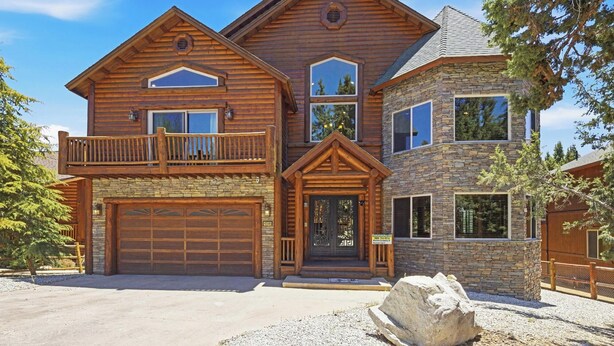 A two-story log cabin with a stone facade, a garage, and a balcony. - Luxury! 3 Master Suites! Located Near the Lake! Pool Table! Propane BBQ! (Big Bear City)
