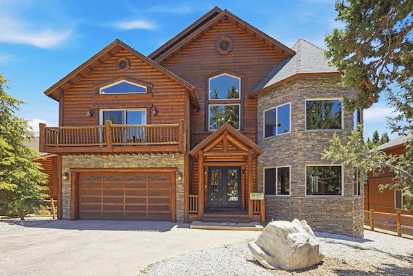 Eine zweistöckige Blockhütte mit Steinverkleidung, einer Garage und einem Balkon.