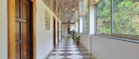 A hallway with a checkered floor, wooden doors, and a window with a view of greenery.