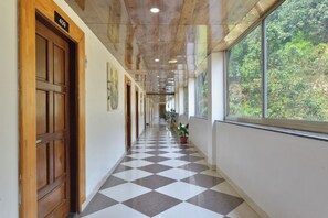 Un couloir doté d’un sol à carreaux, de portes en bois et d’une fenêtre donnant sur un paysage verdoyant.