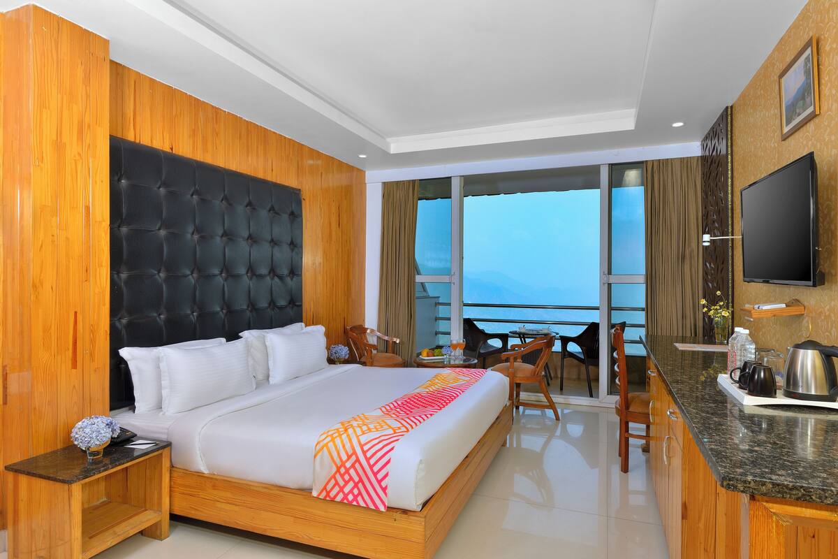 A hotel room with a large bed, a wooden headboard, a dining area, a kitchen counter, and a TV.