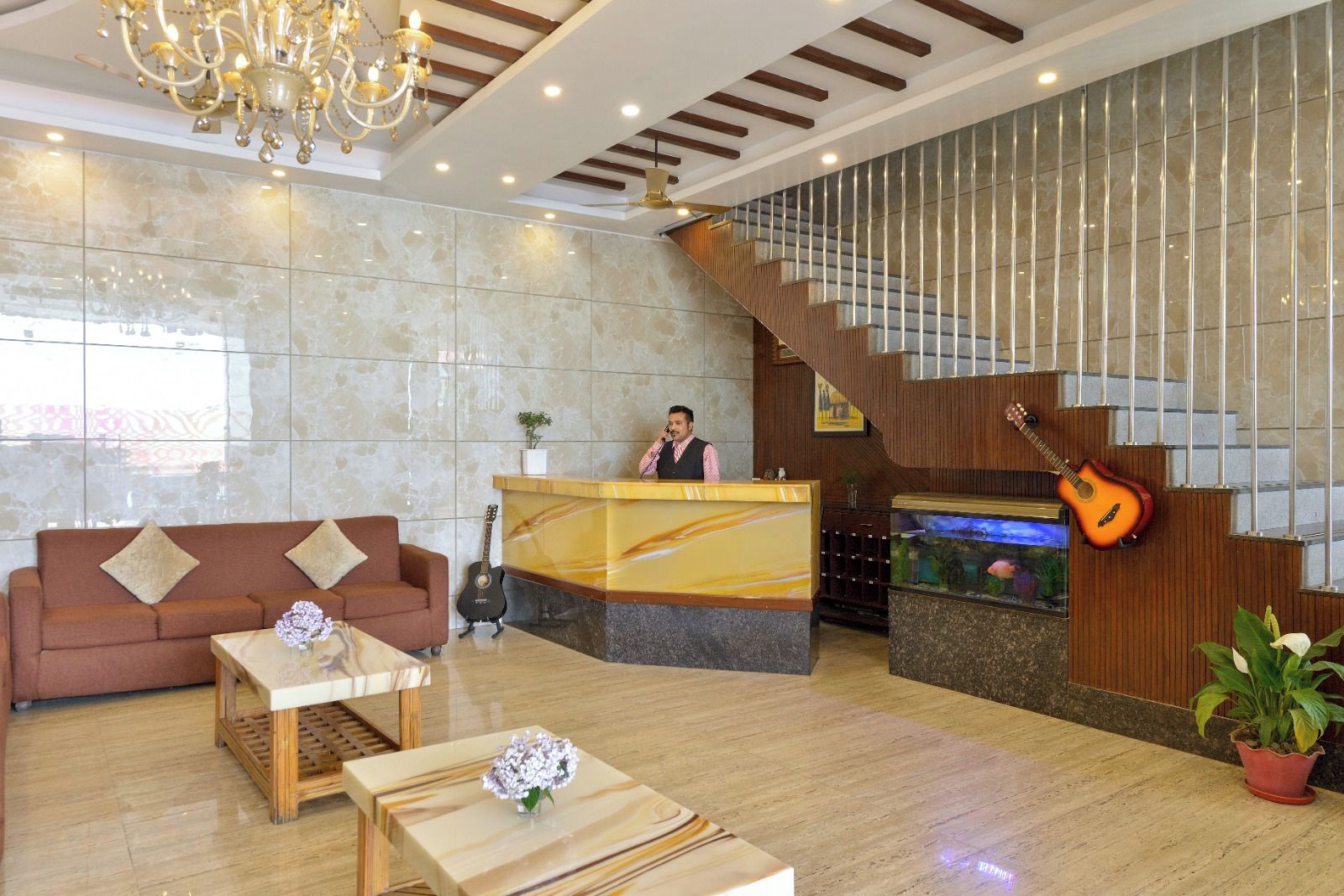 A hotel lobby with a reception desk, a staircase, a sofa, a coffee table, and a guitar.