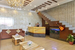 A hotel lobby with a reception desk, a staircase, a sofa, a coffee table, and a guitar.
