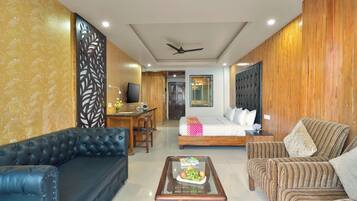 A hotel room with a bed, a sofa, a coffee table, a TV, and a ceiling fan.