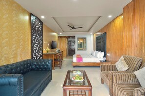 A hotel room with a bed, a sofa, a coffee table, a TV, and a ceiling fan. - Ginger Lansdowne, Mall Road (Lansdowne)