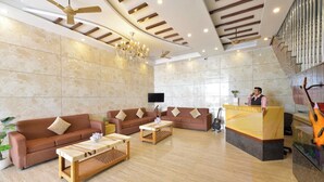 Um hall amplo com design moderno, incluindo área de estar com sofás e uma mesa de centro, palco com suporte para microfone e um violão.