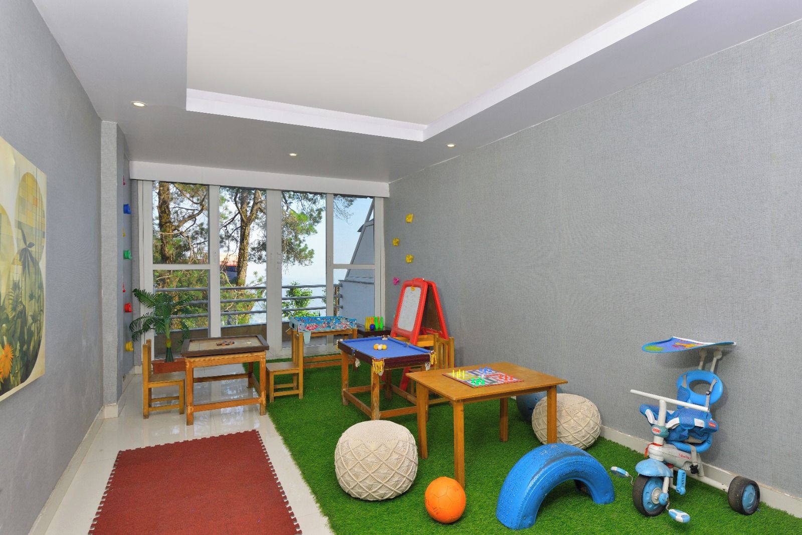 A children's playroom with a pool table, a small table with toys, a tricycle, and a red easel.