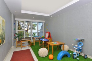 Ein Spielzimmer für Kinder mit Billardtisch, einem kleinen Tisch mit Spielzeug, einem Dreirad und einer roten Staffelei.