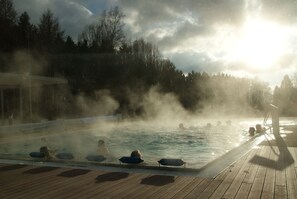 A pool area with people relaxing on lounge chairs, surrounded by trees and steam rising from the water. - Hotel Sockenbacher Hof (Waldbrunn)