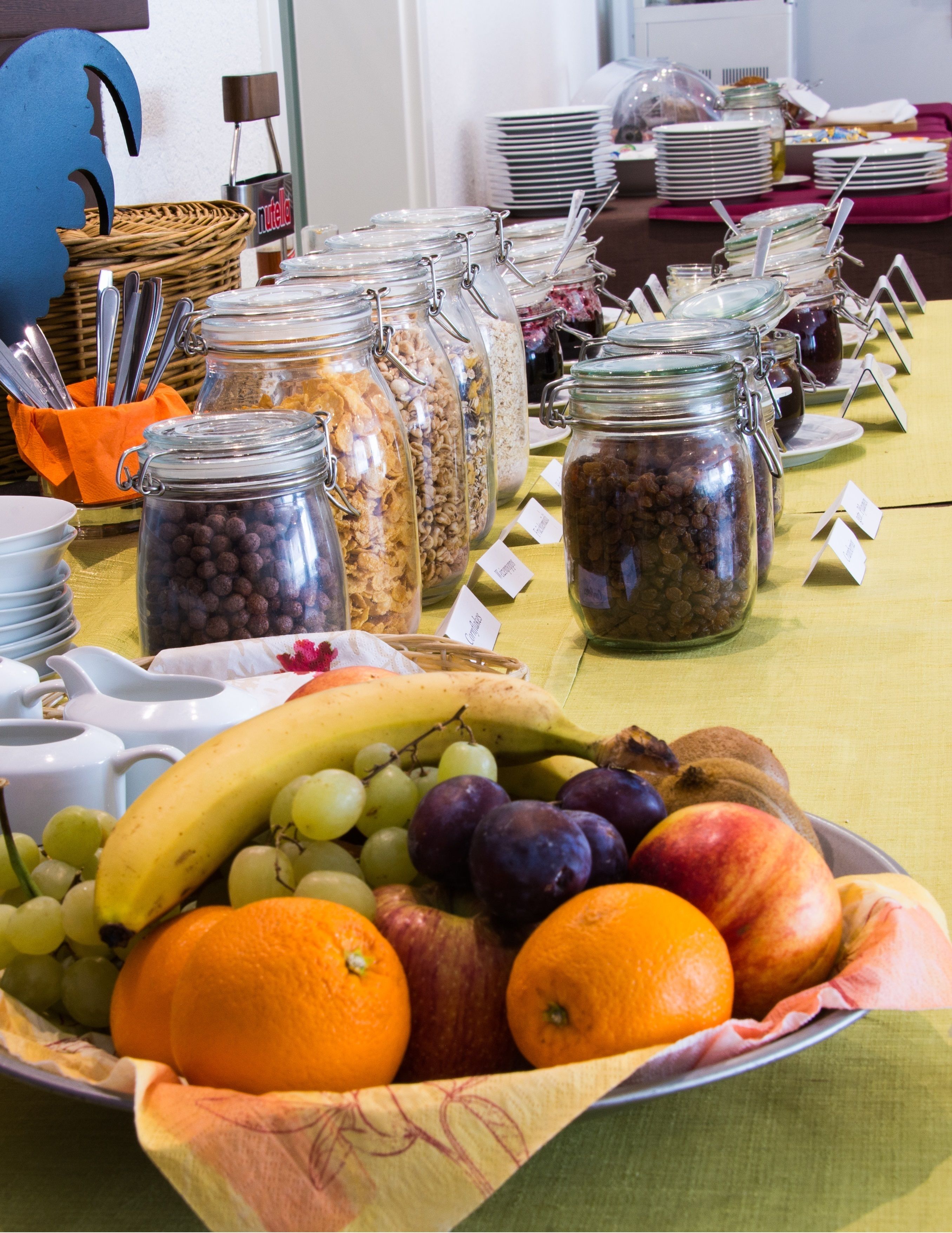 A buffet table with various food items, including fruits and cereals in jars, and a basket of bread.