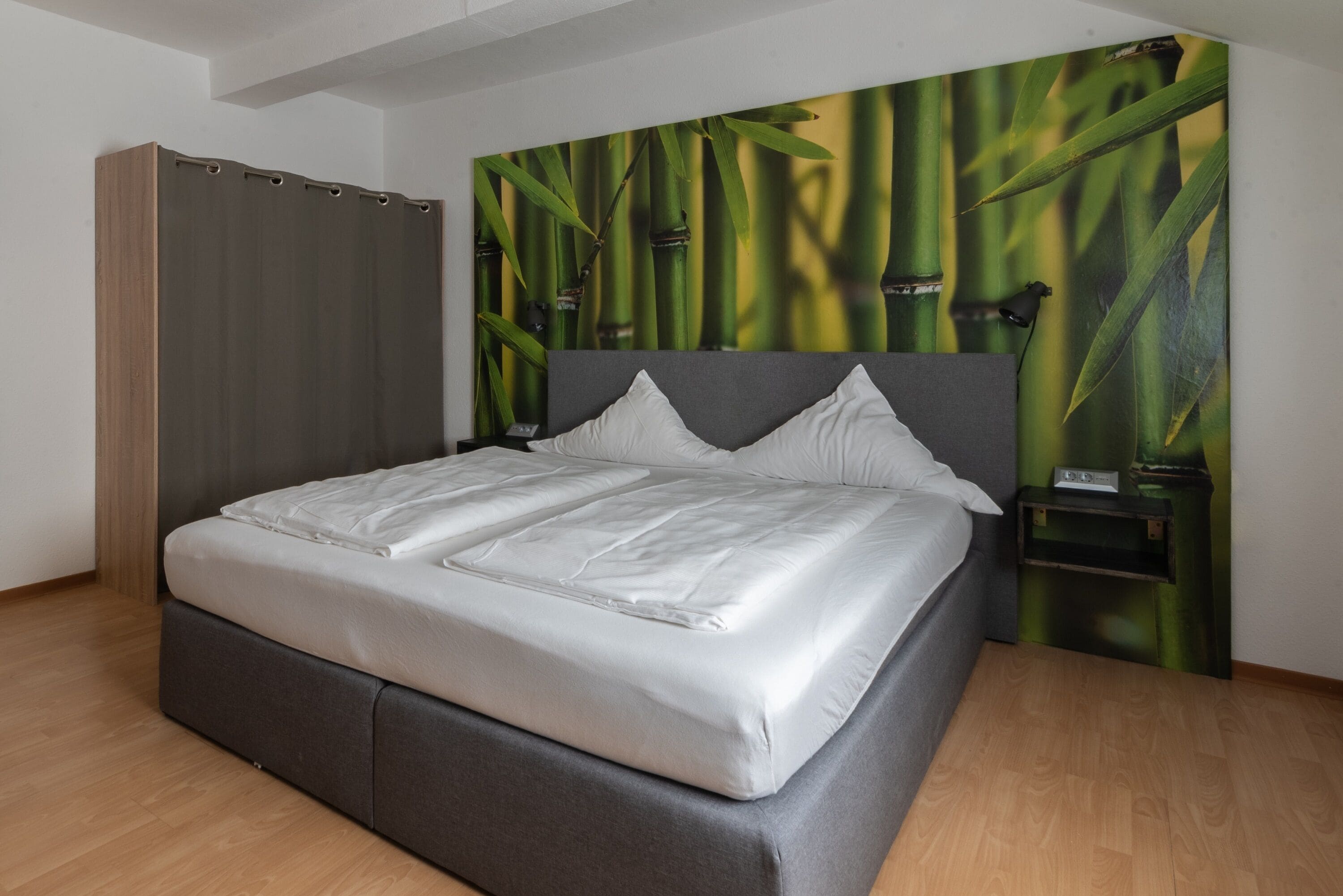 Ein modernes Schlafzimmer mit einem großen Bett, einem grauen Kopfteil und einer Wandmalerei von Bambus.