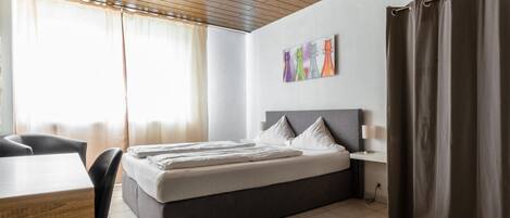 Une chambre d’hôtel moderne avec un grand lit, un bureau et une fenêtre avec des rideaux.