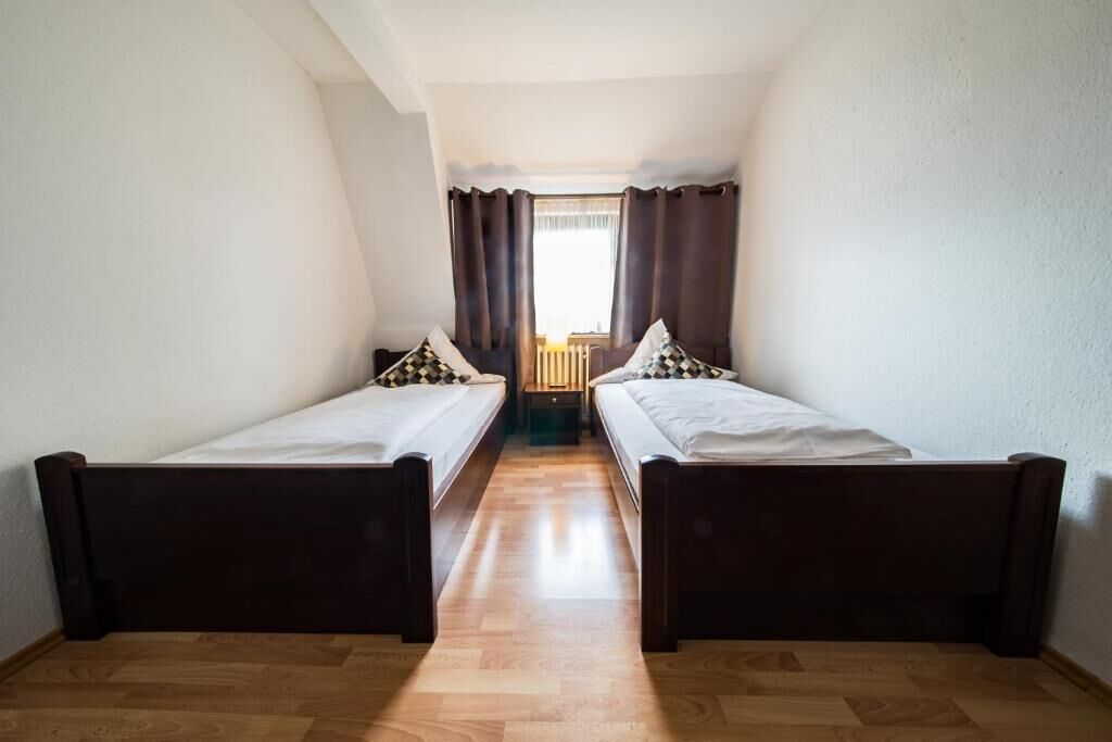 A room with two single beds, wooden flooring, and a window with curtains.