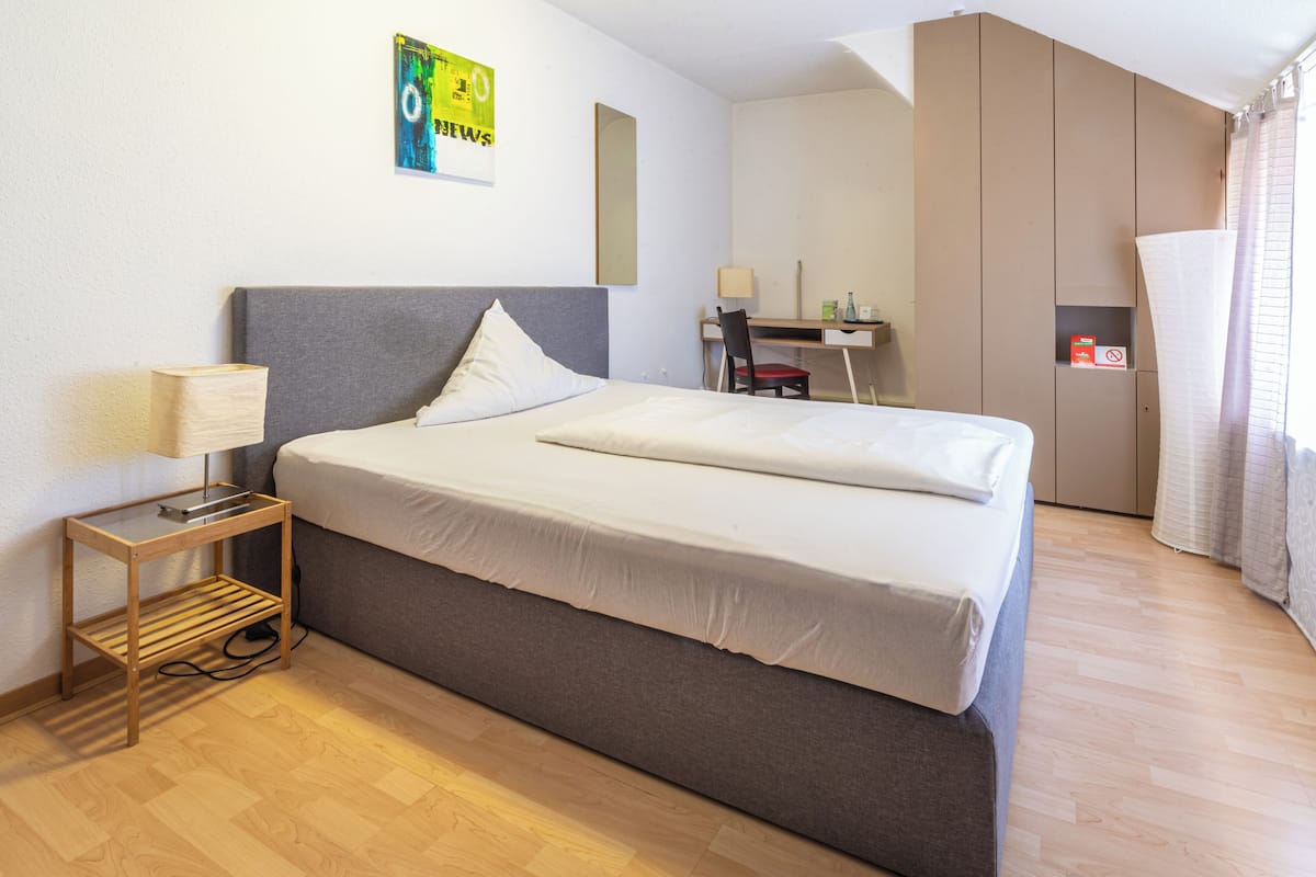 A modern hotel room with a large bed, a desk, and a wardrobe.