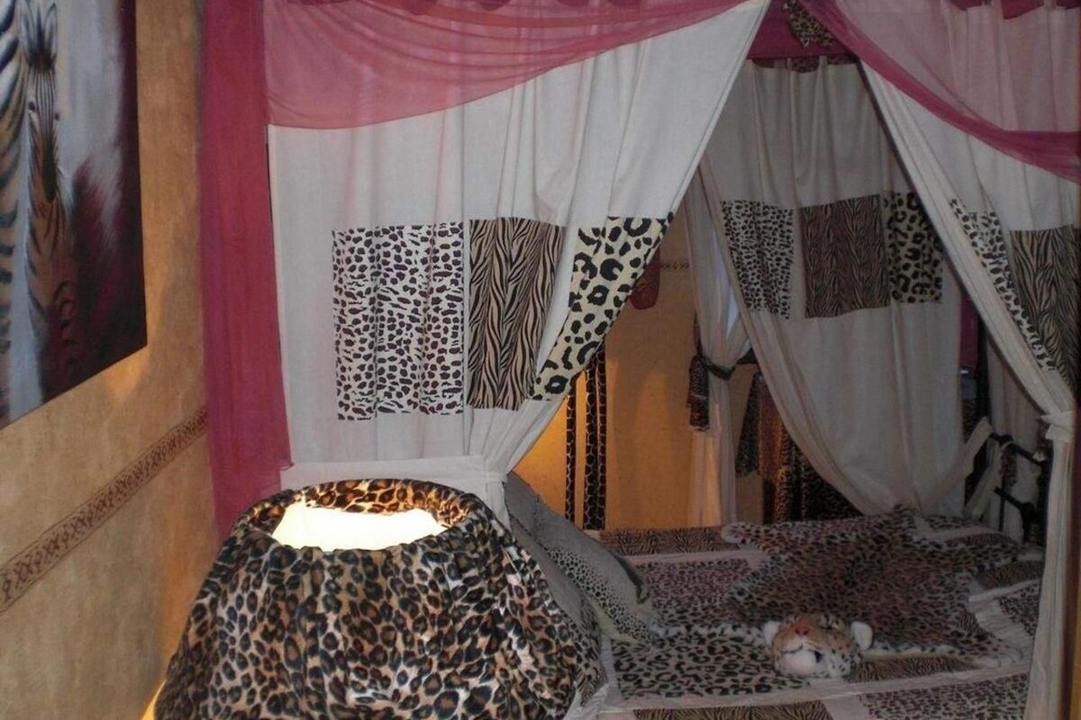 Ein Zimmer mit einem Bett mit Leopardenmuster, einem Himmelbett mit einem gemusterten Vorhang und einer Wand mit einem großen Gemälde.