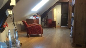Un loft spacieux avec un plancher en bois, un fauteuil rouge, un coin repas avec une table en bois et une bibliothèque.