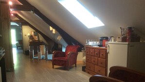 Une pièce mansardée chaleureuse, avec un plancher en bois, un fauteuil rouge, une commode en bois et un puits de lumière.