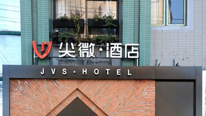 L’extérieur de l’hôtel JVS présente une façade en briques, une entrée bien dégagée et une enseigne au-dessus de la porte.