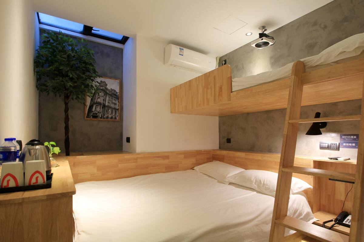 Een kleine hotelkamer met een stapelbed, een bureau met voorzieningen, een wandairconditioner en een klein raam met uitzicht.
