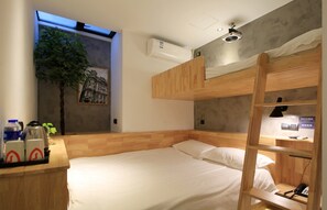 A compact hotel room with a bunk bed, a desk with amenities, a wall-mounted air conditioner, and a small window with a view.