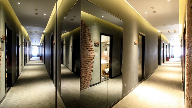 Un couloir d’hôtel moderne avec des murs recouverts de miroirs, un mur d’accent en briques et un long couloir menant à plusieurs portes.