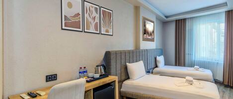 A hotel room with a desk, two beds, a refrigerator, and artwork on the wall.