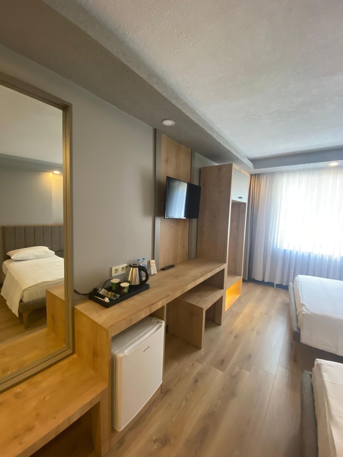 Une chambre d’hôtel avec un bureau en bois, un lit, un petit réfrigérateur, un téléviseur fixé au mur et un grand miroir.