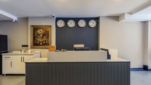 A reception area with a modern design, featuring a central counter, a wall-mounted clock, and a decorative painting. - Evim Hotel (Corlu)