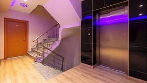A modern interior with a wooden door, a staircase, and a metallic elevator. - Evim Hotel (Corlu)