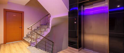 A modern interior with a wooden door, a staircase, and a metallic elevator.