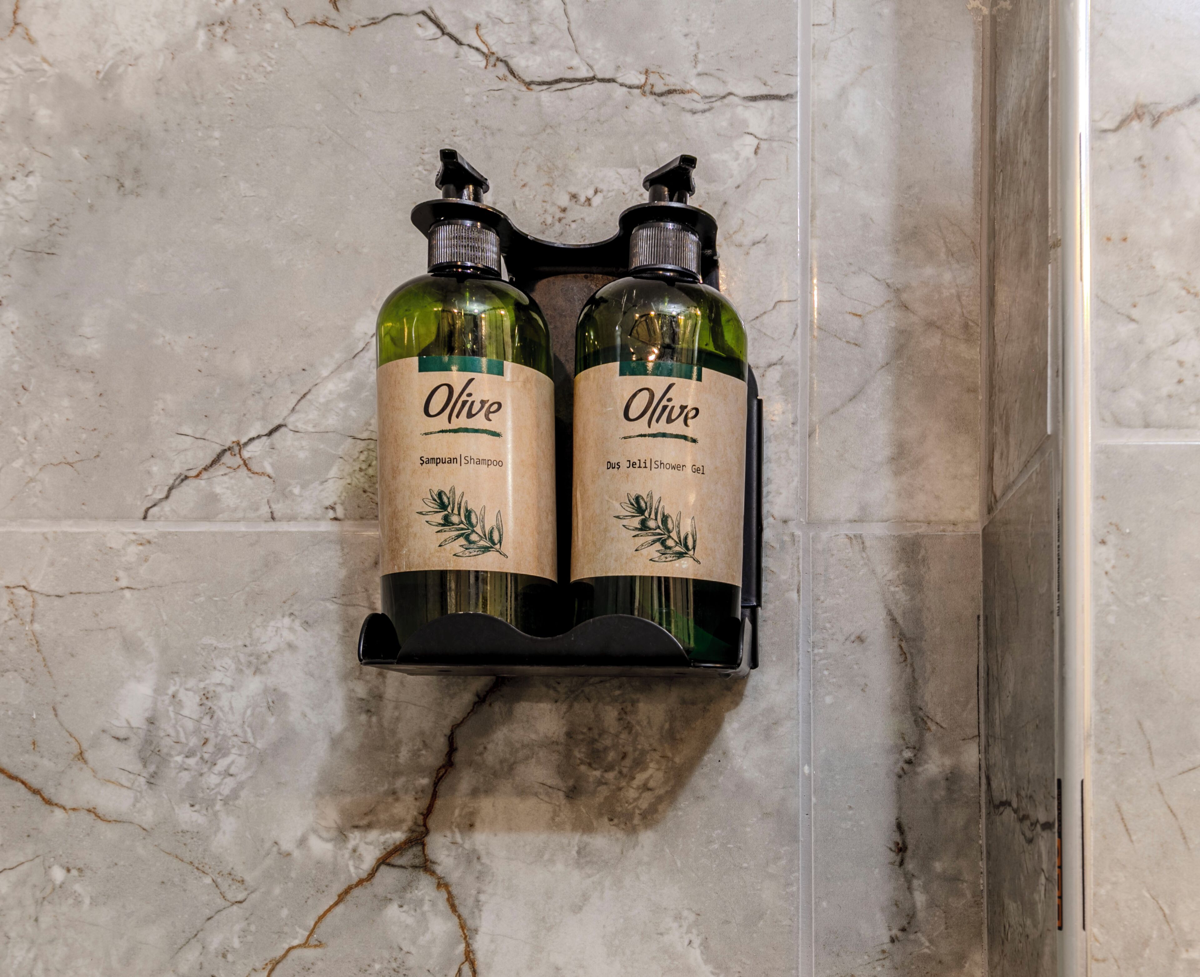 Duas embalagens de shampoo e gel de banho Olive sobre uma parede de mármore.