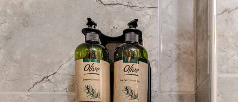 Duas embalagens de shampoo e gel de banho Olive sobre uma parede de mármore.