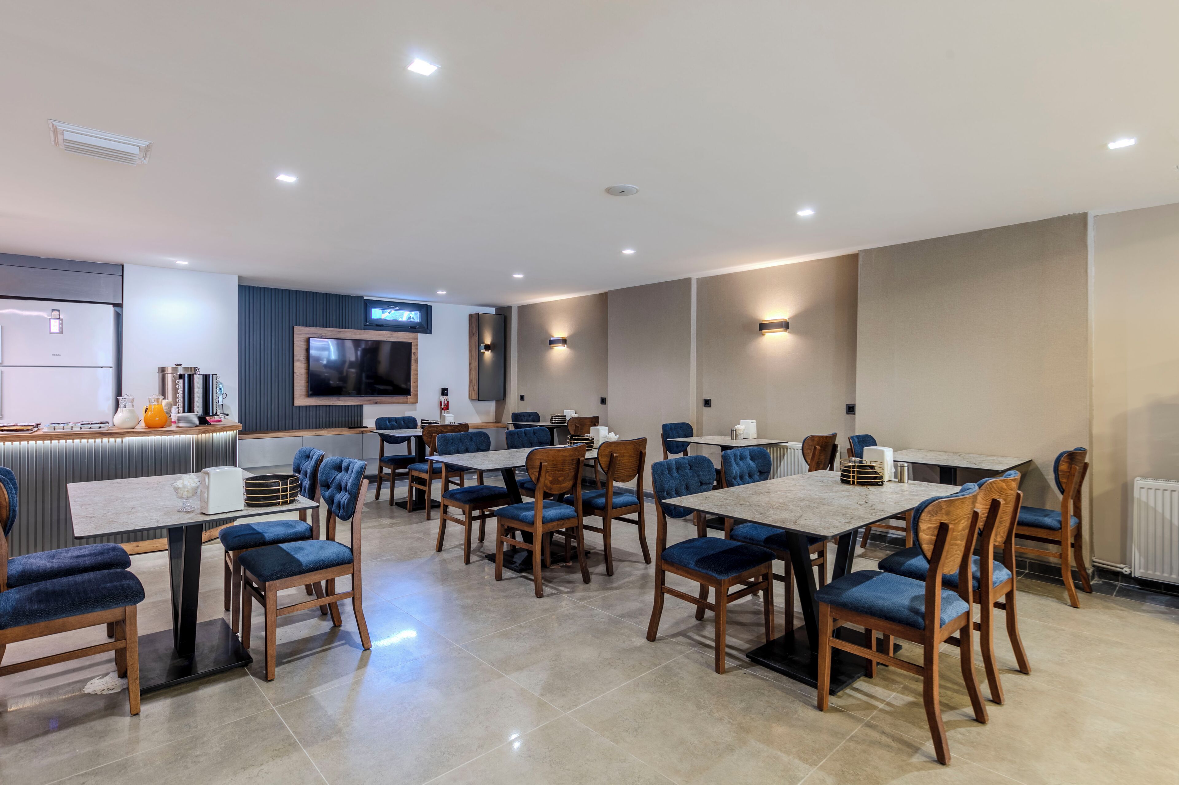 Un comedor moderno con varias mesas y sillas, una encimera de cocina y un televisor montado en la pared.