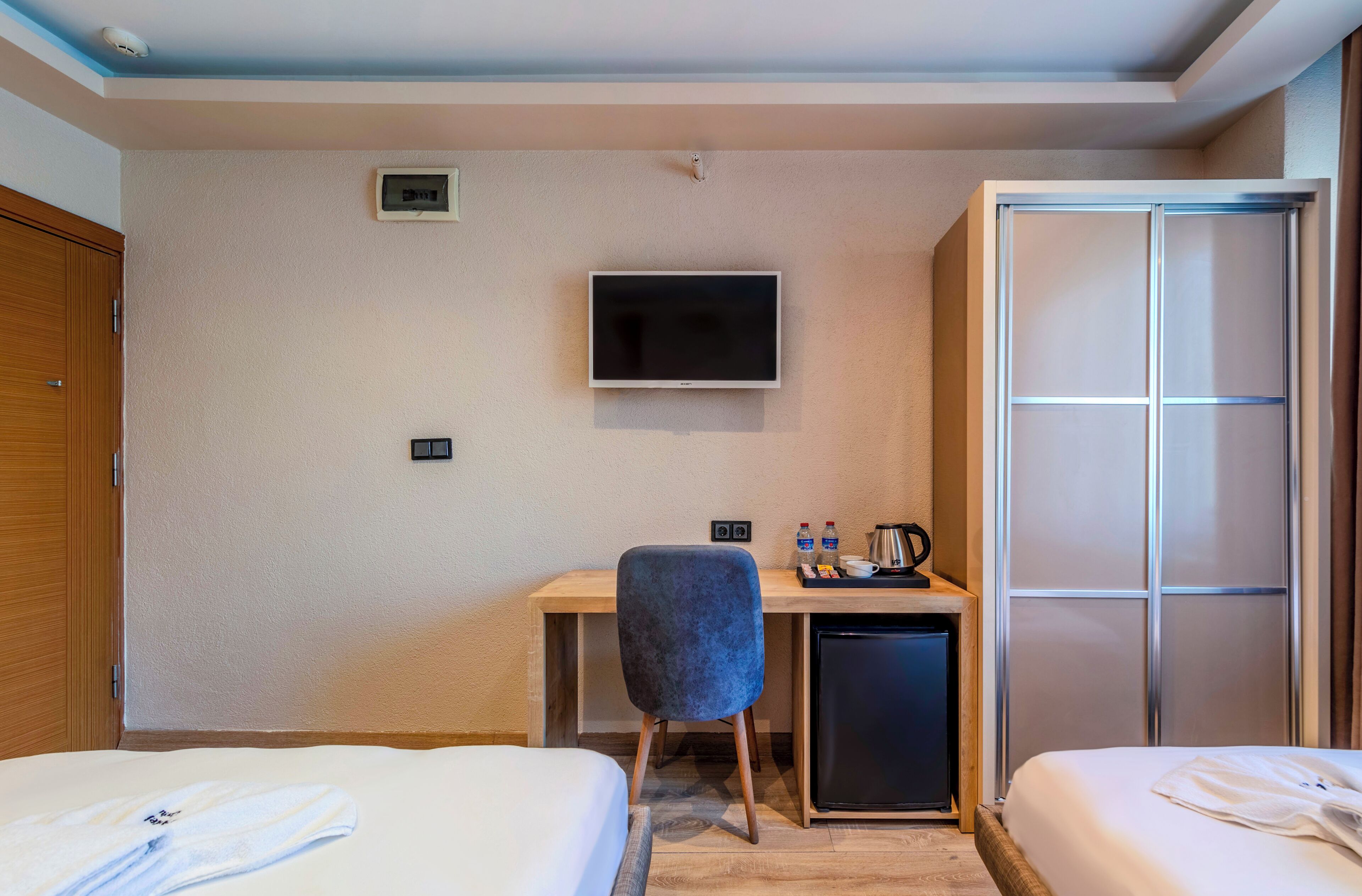Habitación de hotel con dos camas, un escritorio con silla, televisor, minibar y armario.