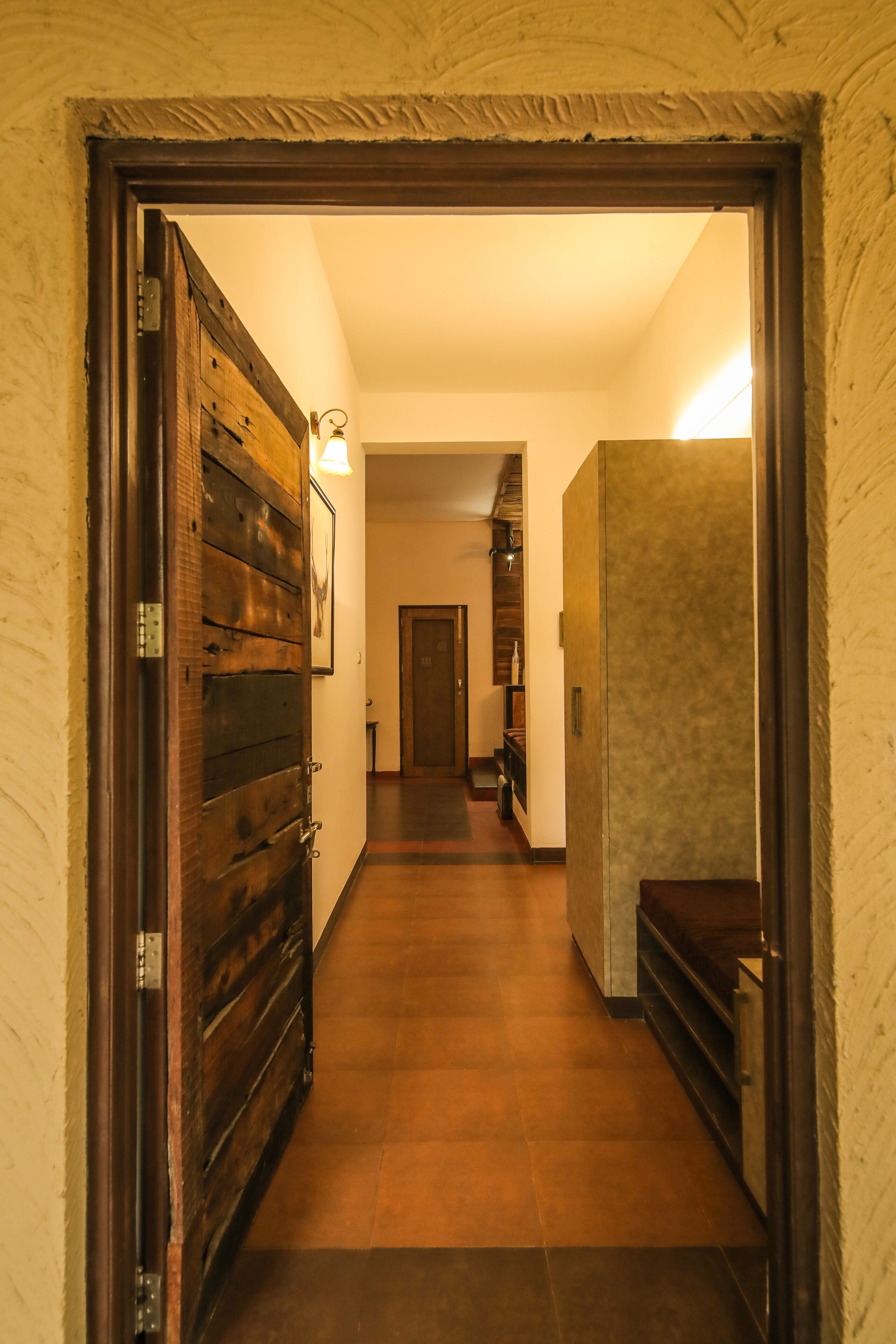 Un pasillo con una puerta de madera a la izquierda, una lámpara encima y otra puerta al final.