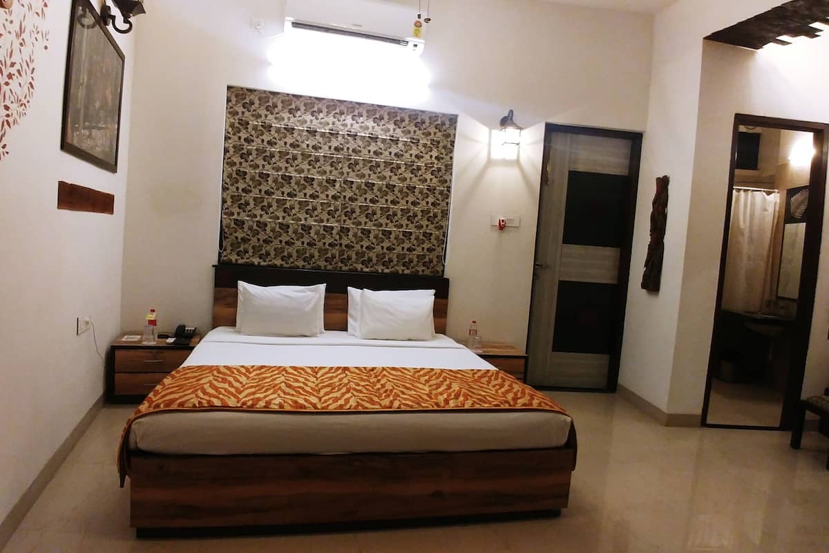 A bedroom with a bed, a nightstand, a wall-mounted light, a mirror, and a door leading to another room.