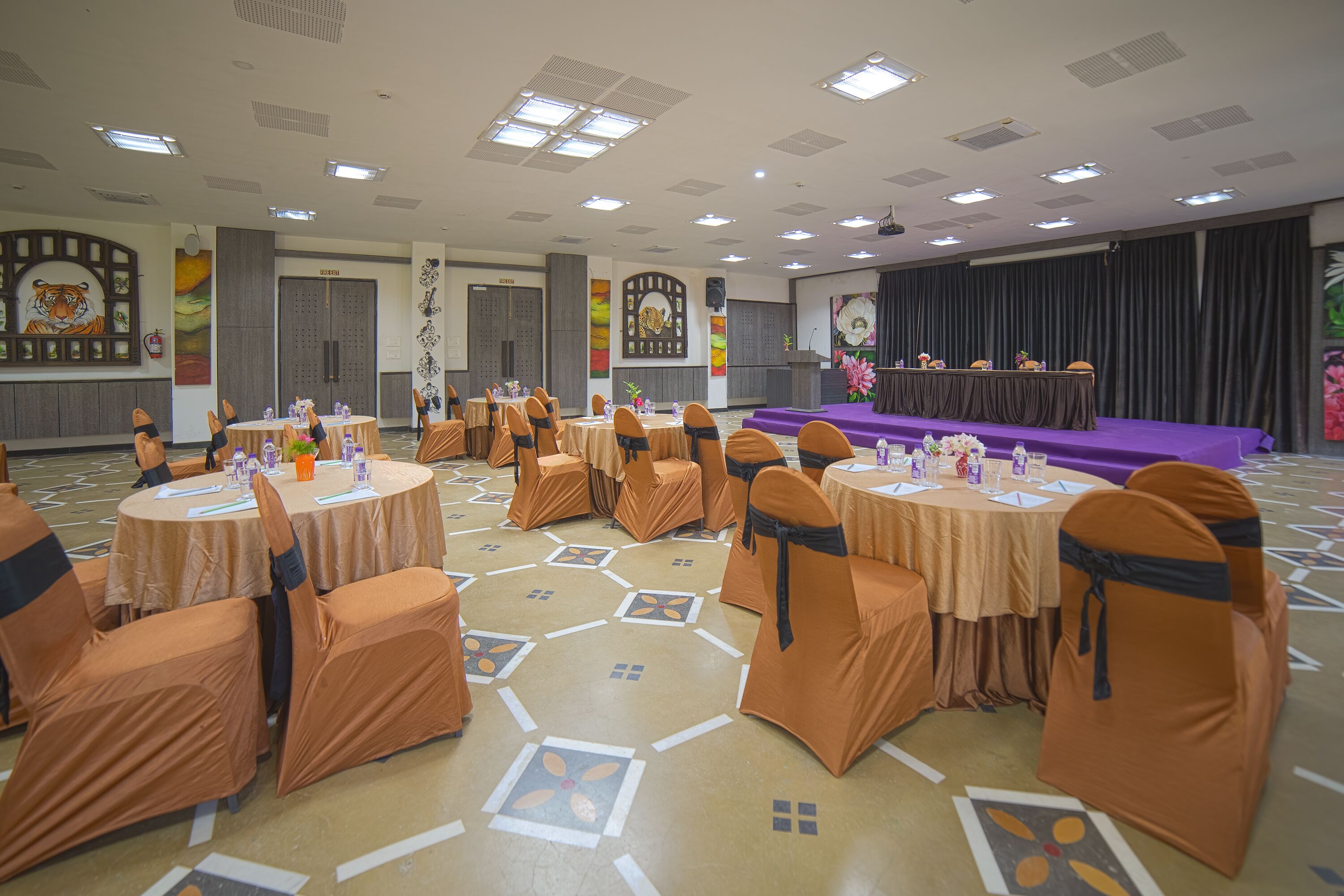 A banquet hall with round tables, orange chairs, and a stage with a purple backdrop.