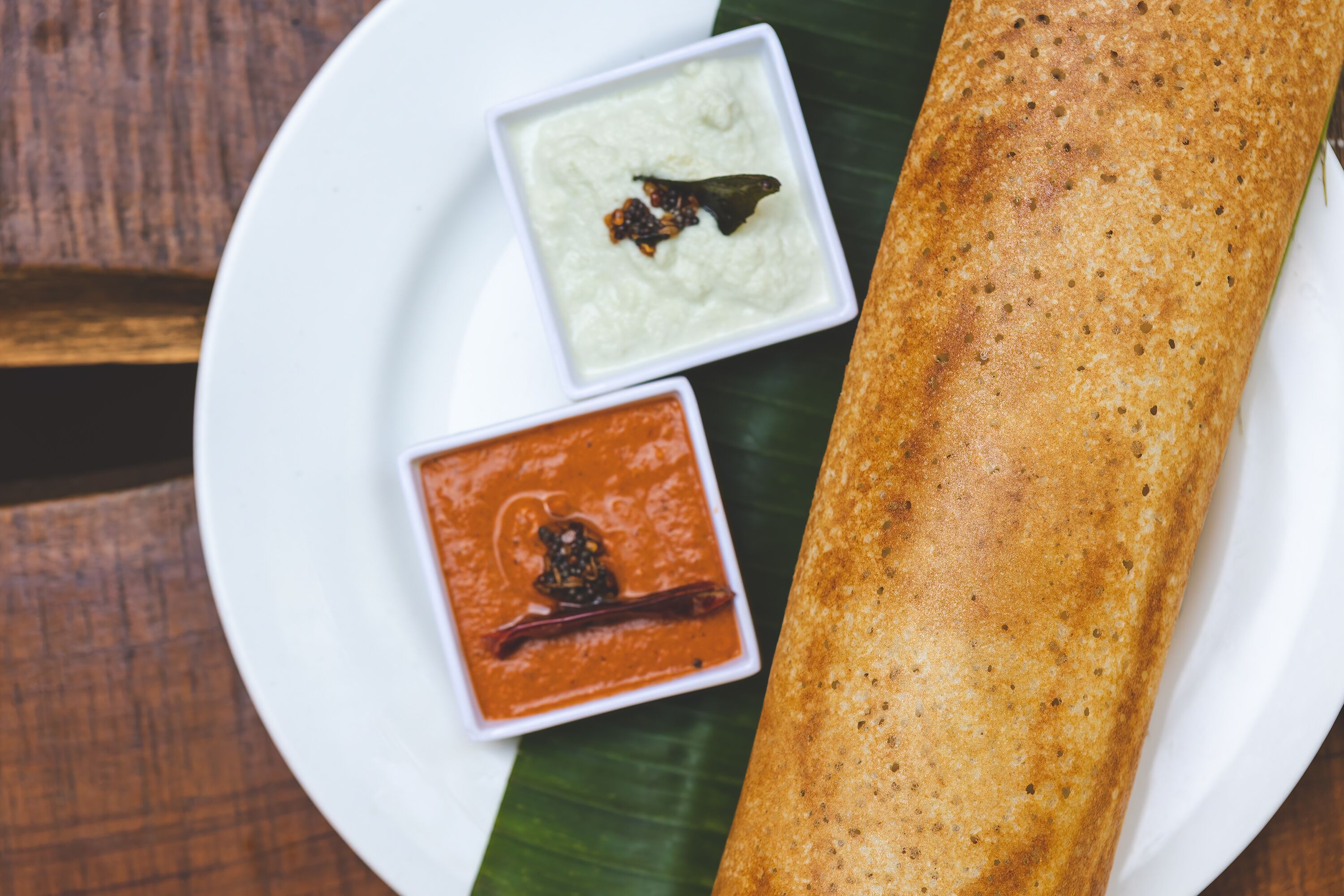 A plate with a dosa, coconut chutney, and tomato chutney.
