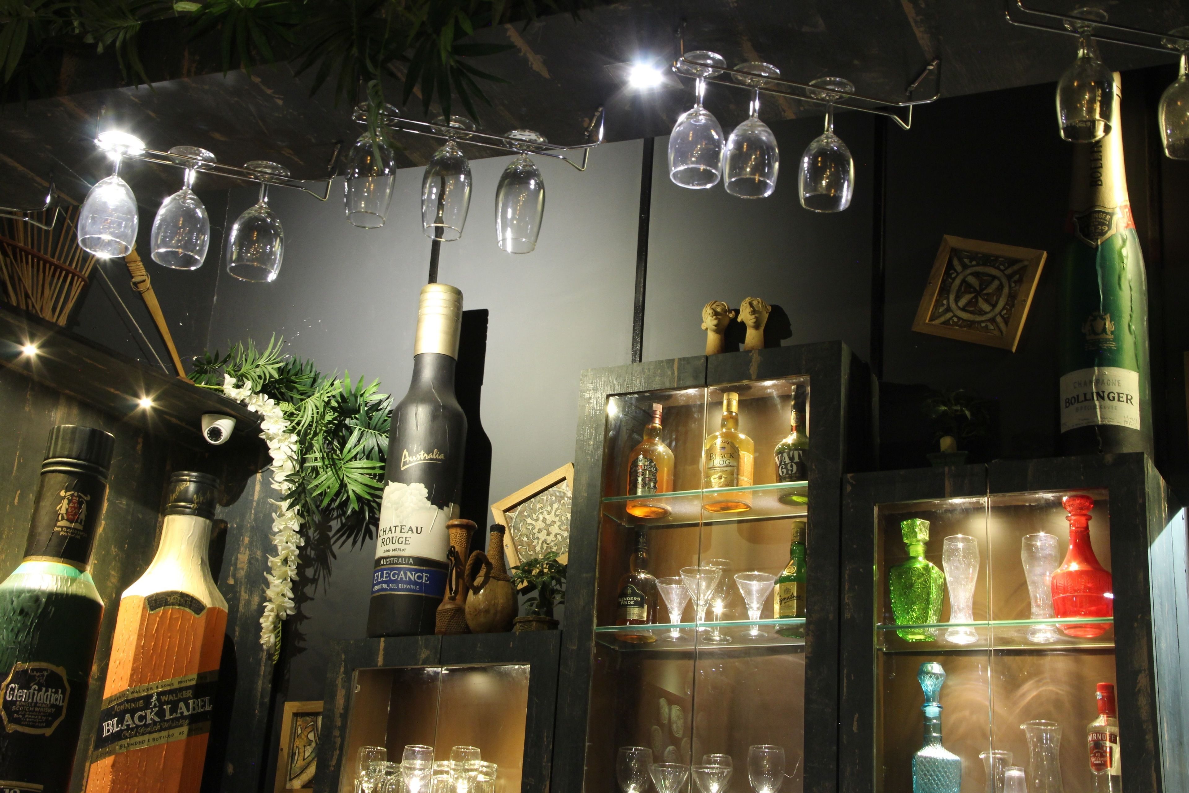 Eine Bar mit verschiedenen Flaschen und Gläsern, darunter eine Champagnerflasche und mehrere leere Weingläser, die an der Decke hängen.