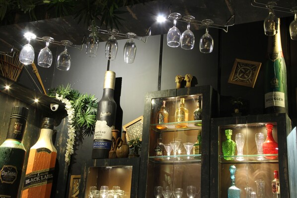 A bar area with various bottles and glasses, including a bottle of champagne and several empty wine glasses hanging from the ceiling. - Tathastu Pench (Kurai)