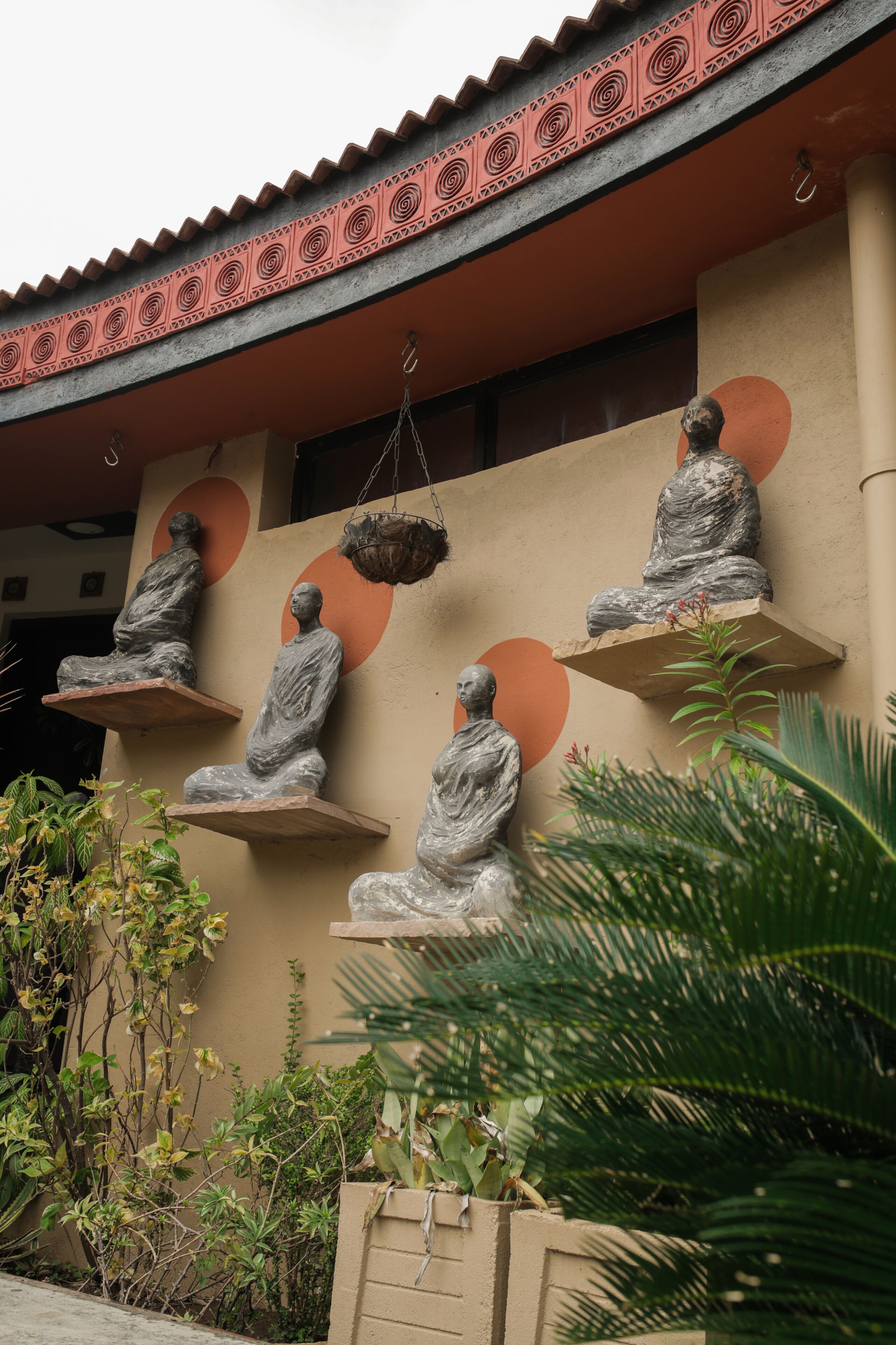 A building facade with four stone Buddha statues on shelves, surrounded by greenery.