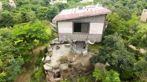 Una casa en los árboles con techo rojo, construida en una formación rocosa rodeada de exuberante vegetación.