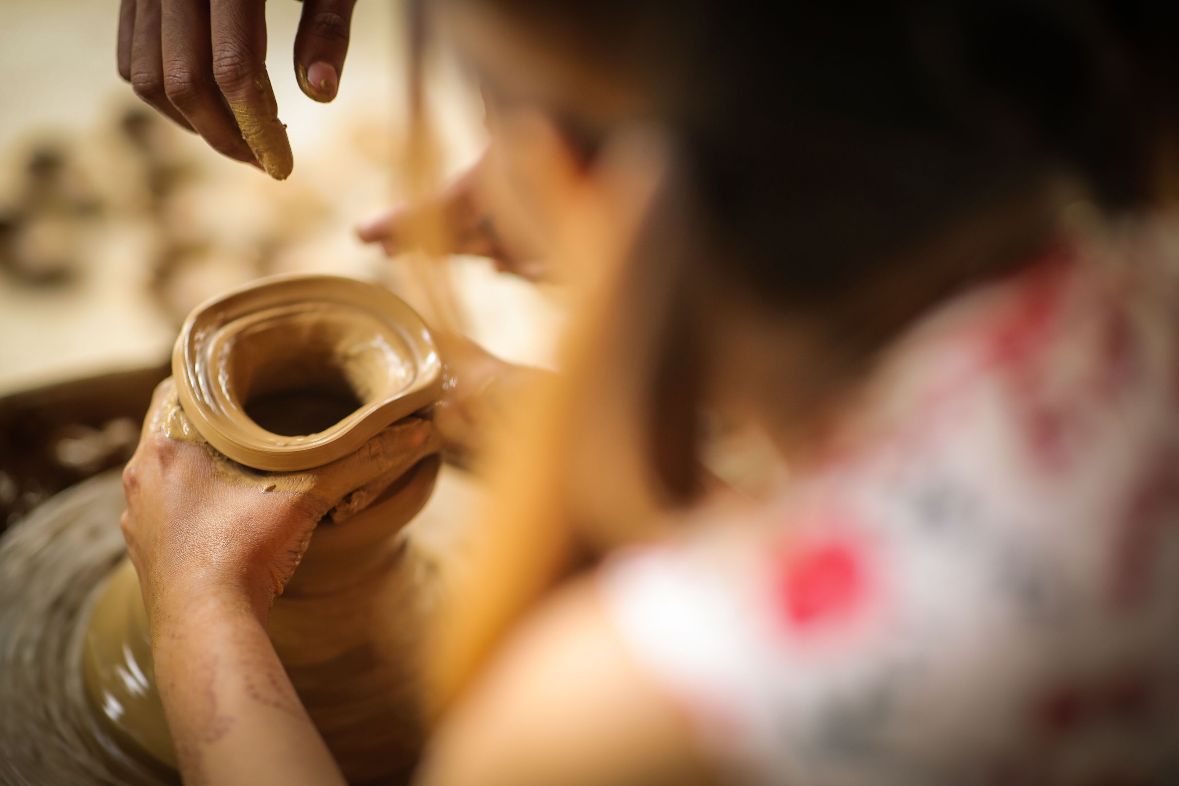 A person shaping a clay pot on a pottery wheel.