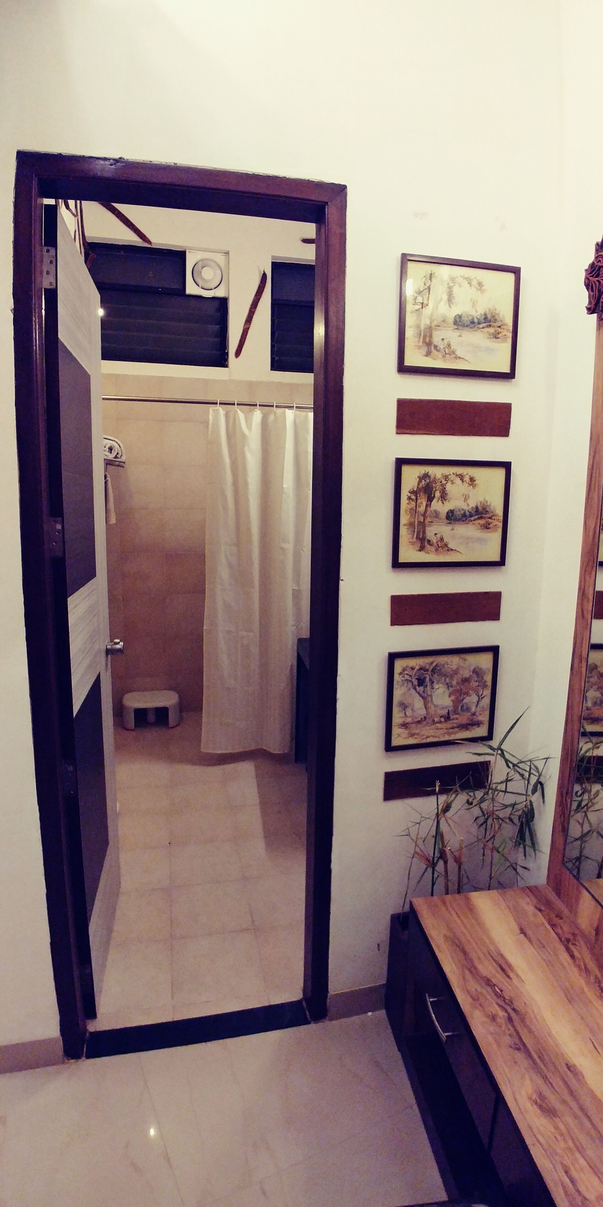 Ein Badezimmer mit Dusche, Toilette und einer kleinen Stehgehilfe. An der Wand hängen gerahmte Bilder.