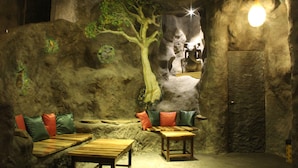 Un interior que recuerda a una cueva, con un banco de madera, una mesa y un mural con un árbol.