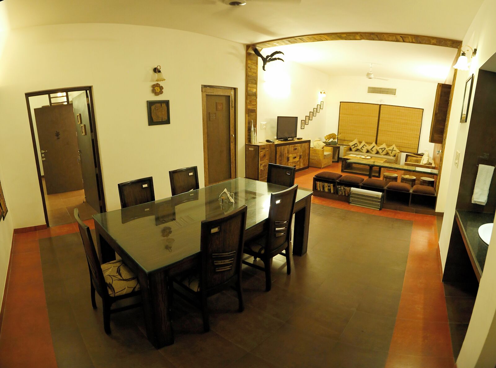 Un coin repas avec une table en verre et des chaises en bois, un salon avec un canapé et un téléviseur, et une salle de bain avec des toilettes et un lavabo.