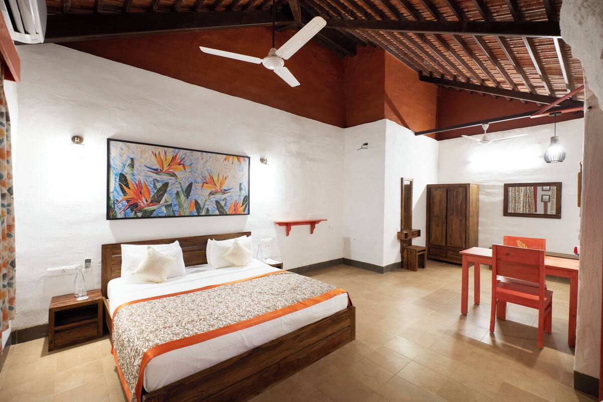 A bedroom with a wooden bed, a desk, a chair, a ceiling fan, and a painting on the wall.
